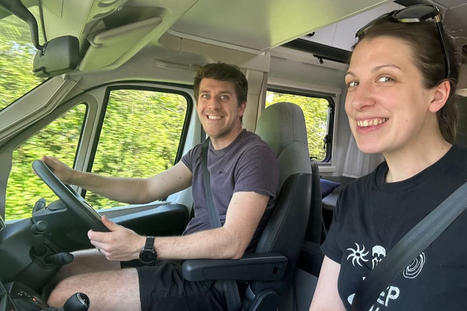 A smiling couple driving a Why Knott motorhome